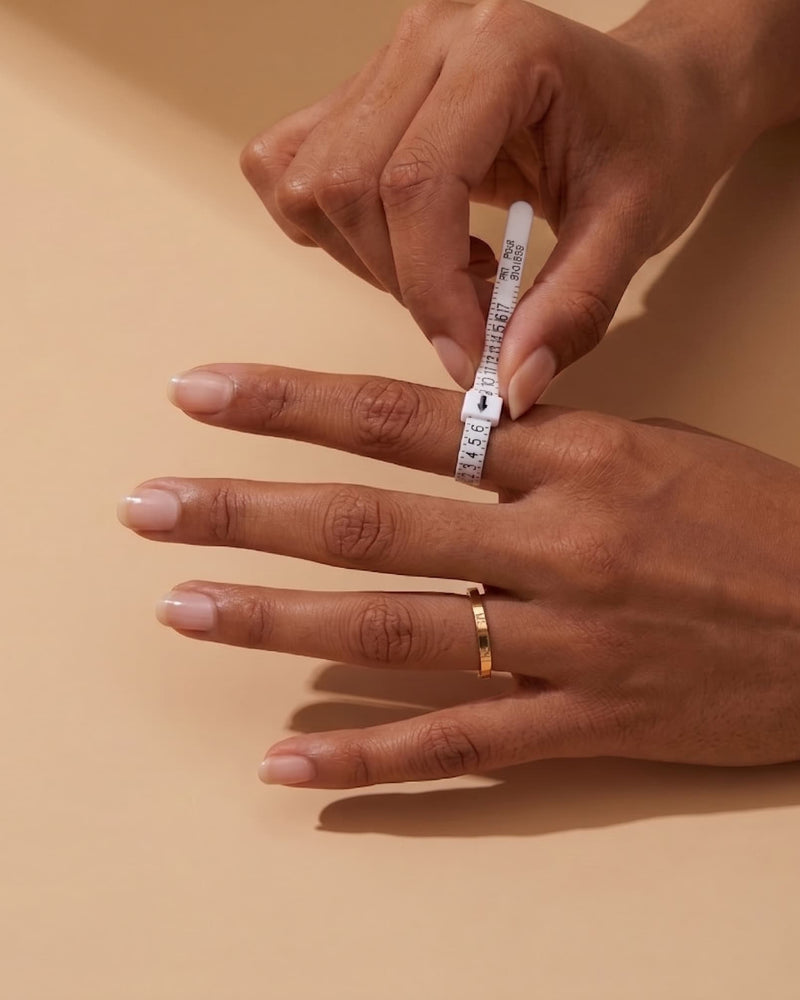Person measuring a ring size with a small ruler on a beige background