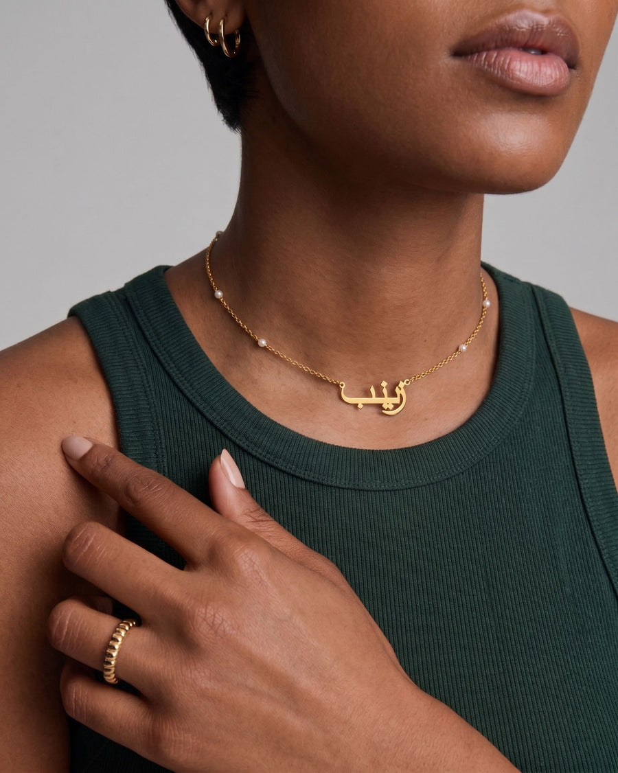 Model Image - Heritage name necklace with a gold-tone script pendant and pearl satellite chain detail worn on model