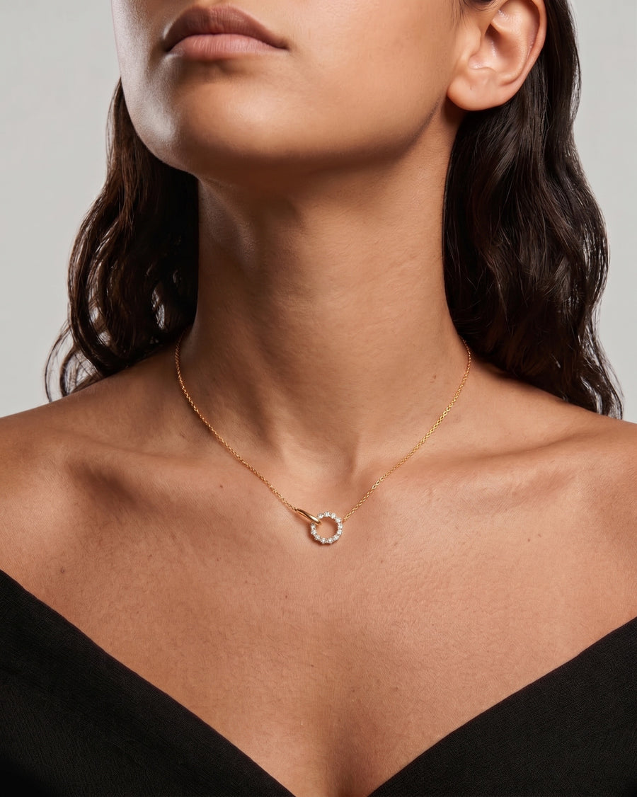 Model image - A close-up of a model wearing a delicate gold chain necklace with a small, open circular pendant adorned with tiny clear stones, set against a neutral gray background.