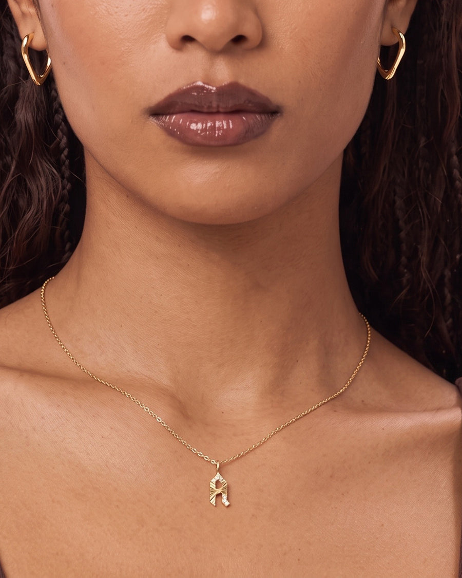 Model image - A close-up of a model wearing a delicate gold chain necklace with a small ribbon-shaped pendant, styled with matching gold hoop earrings.