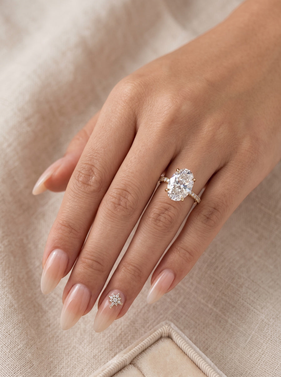 Model image - A close-up of a hand wearing a diamond engagement ring with a pear-cut center stone and a small matching diamond accessory on the middle finger, set against a soft beige fabric background.