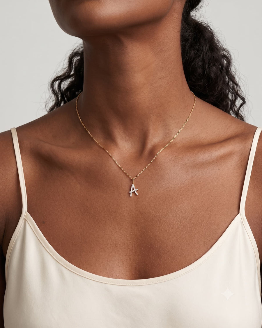 Model image - A close-up of a model wearing a delicate gold chain necklace with a small silver initial 'A' pendant, styled with a cream camisole top against a light gray background.