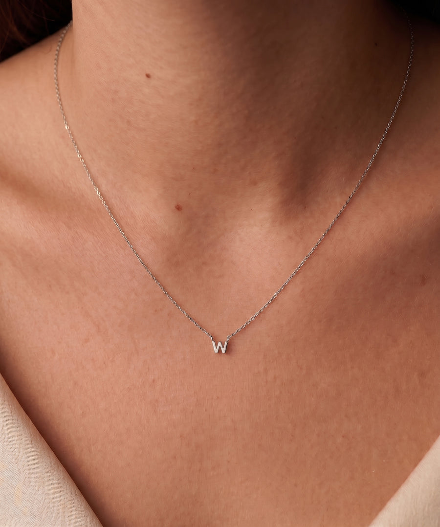 Model Image - A delicate silver chain necklace with a small initial 'W' pendant, worn on the neck of a model.