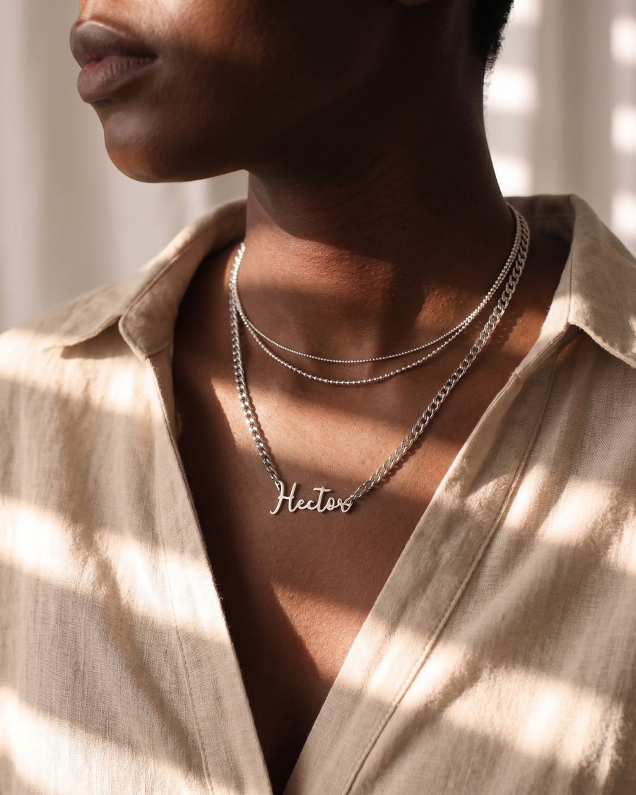 Model Image - personalized script name pendant on a curb chain layered with delicate necklaces worn on model