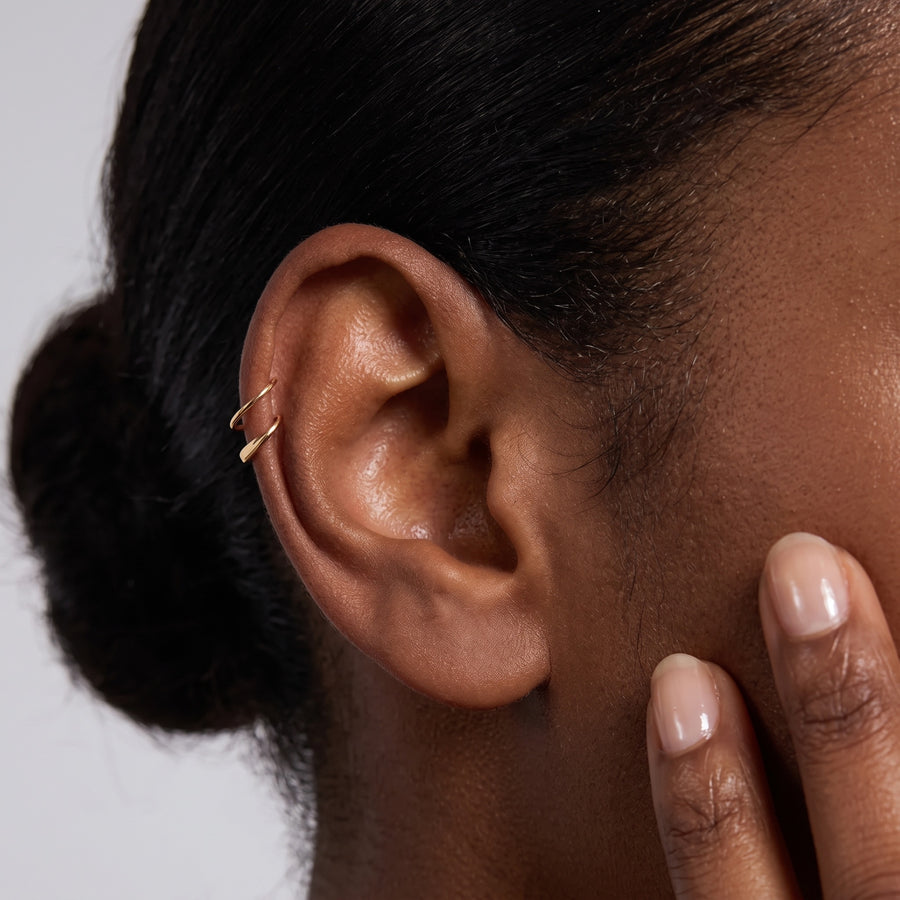 Model image - A close-up of a person's ear wearing a delicate gold ear cuff, with the hand touching the cheek against a light gray background.