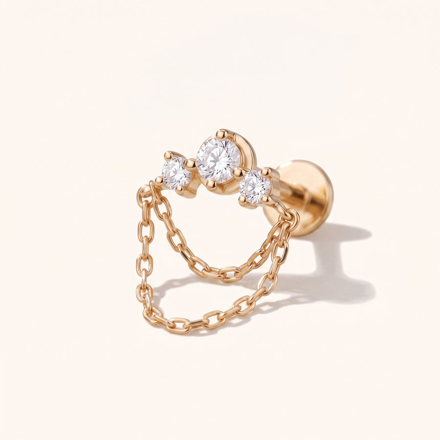 A rose gold double-hoop earring with three clear round-cut gemstones on the front and a delicate chain draped between the hoops, shown on a light cream background.