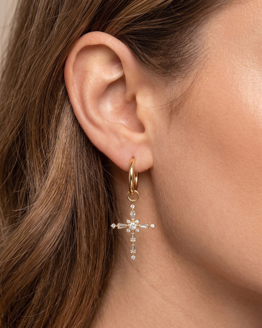 Model Image - Gold-tone hoop earring with dangling CZ cross charm and clear stones on the ear worn on model