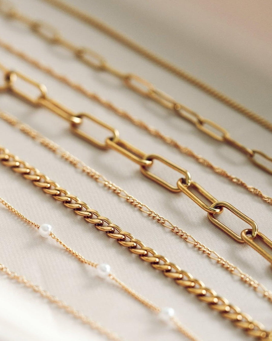 Style Image - Gold plated Figaro bracelet shown layered with assorted chain bracelets on a soft surface