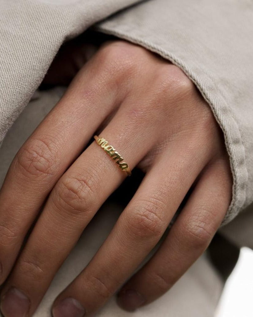 Model Image - gold plated Mama ring with script lettering on a hand partially covered by a neutral sleeve worn on model