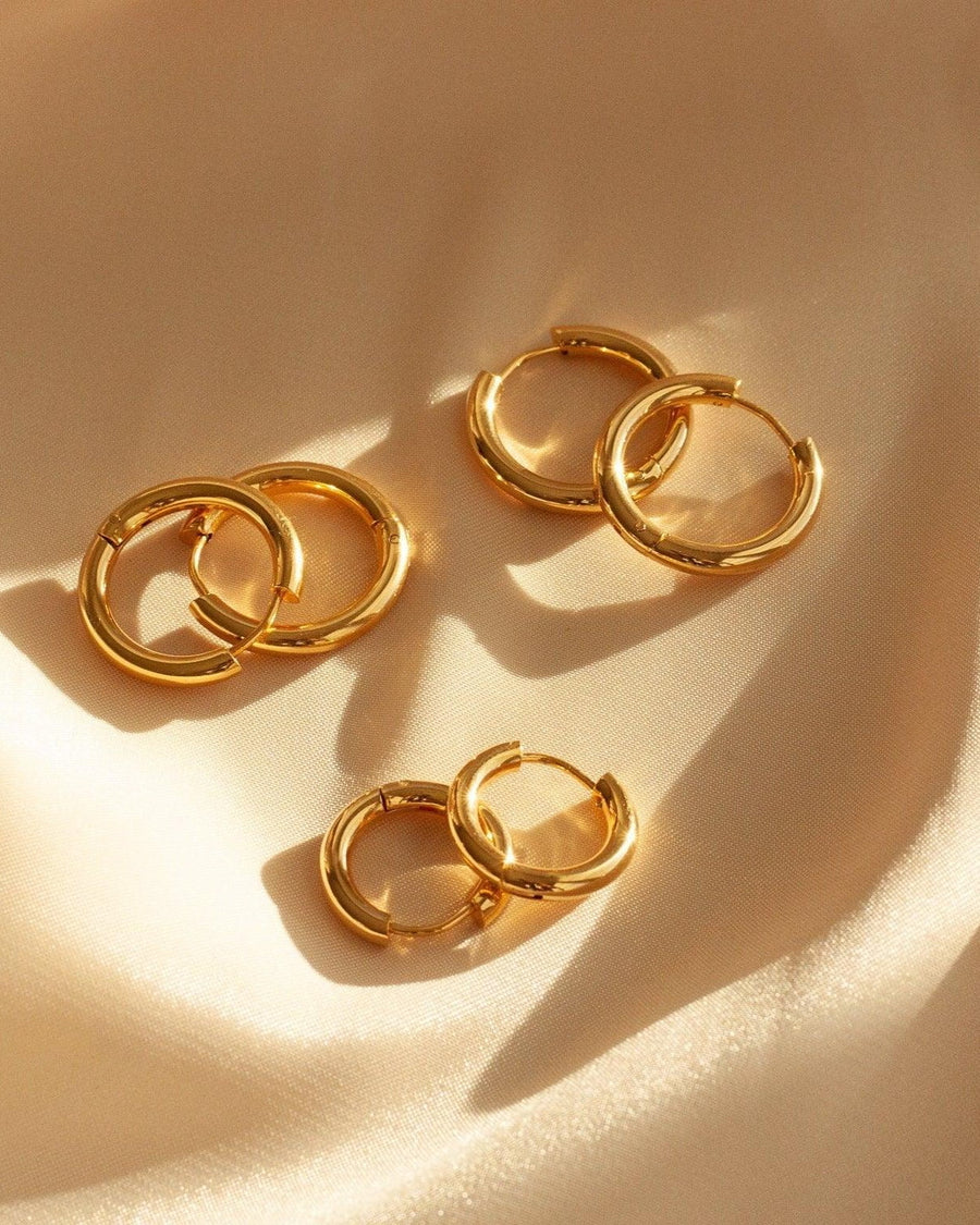 Style Image - Simple 10mm hoop earrings in 18k gold plated stainless steel arranged on soft fabric with warm light