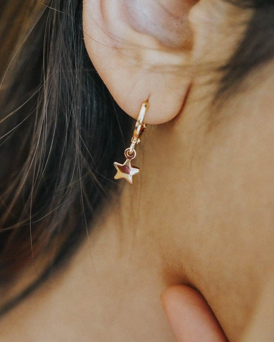 Model Image - Star earring with a small star charm hanging from a hoop worn on model