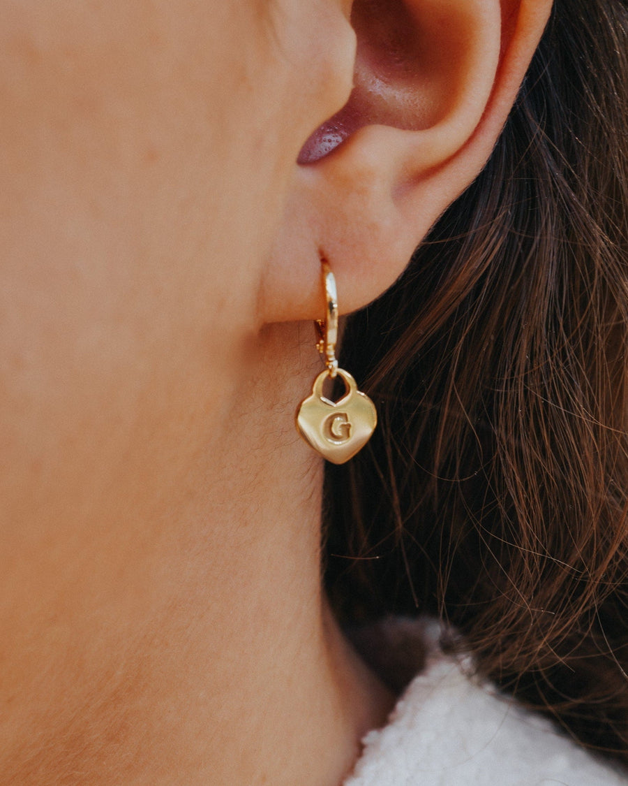 Model Image - 14K gold plated drop hoop earring with a heart pendant and engraved G shown on the ear worn on model