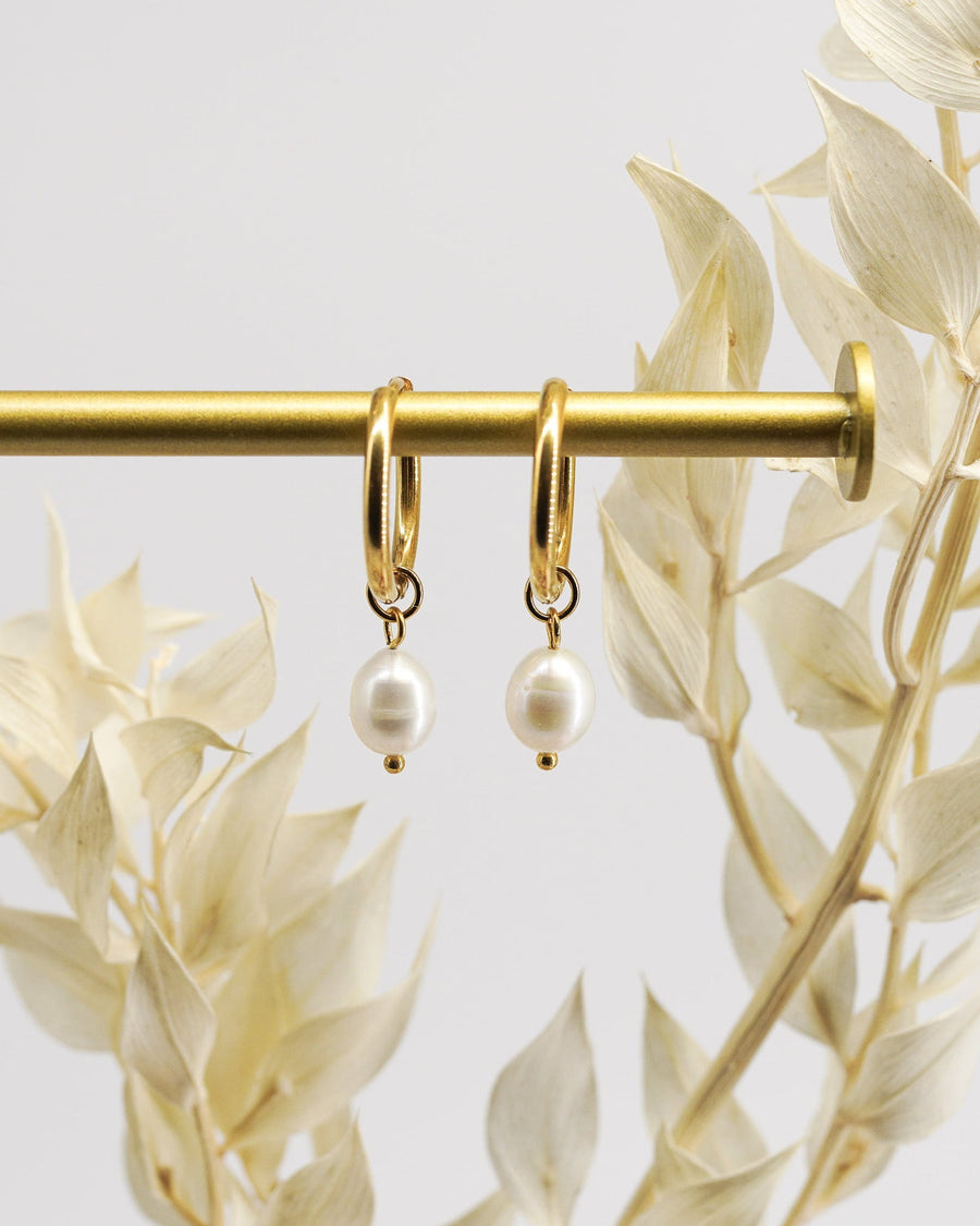 Detail Image - 14K gold plated pearl huggie hoops hanging on a gold bar with pale botanical accents