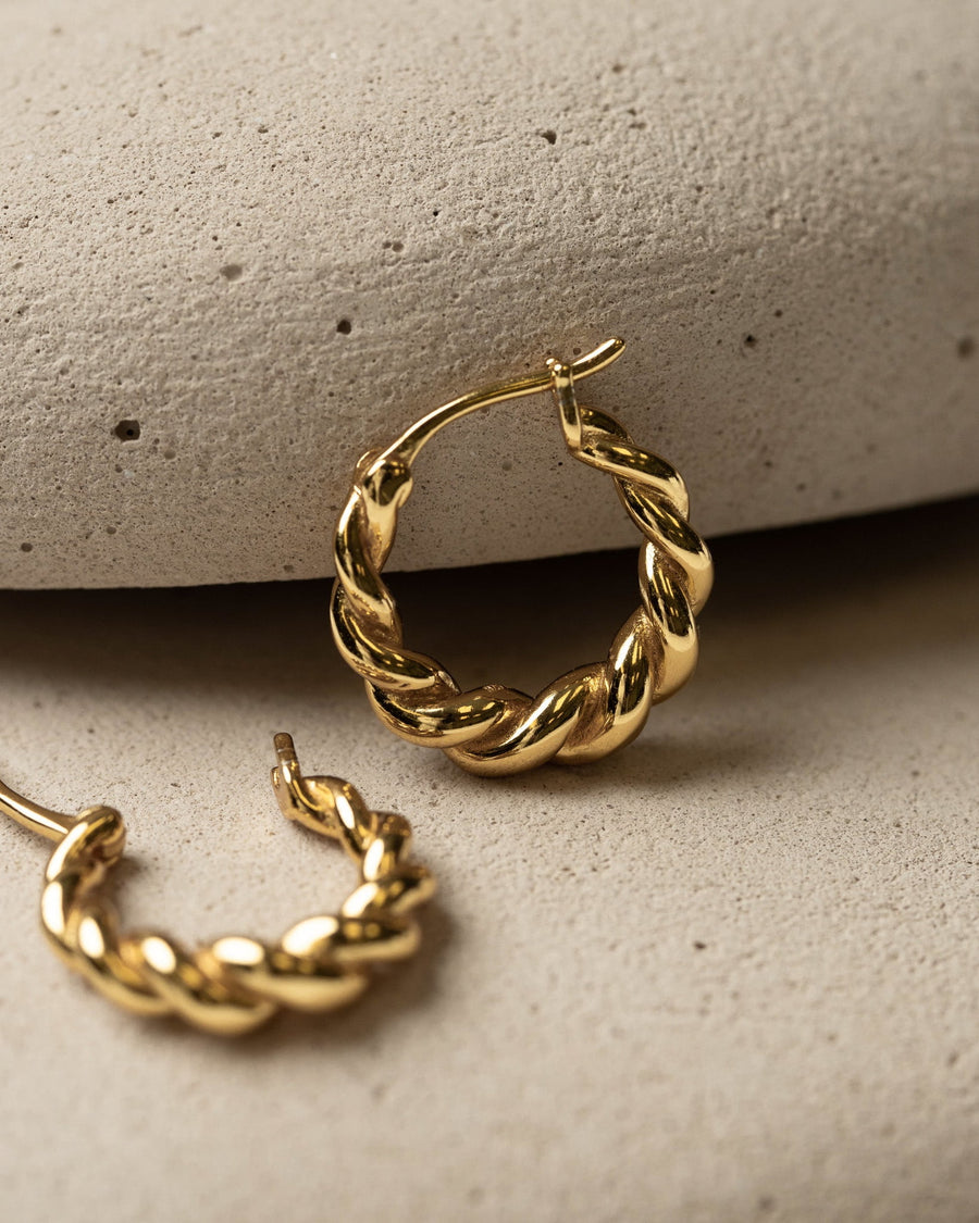 Detail Image - Pair of 14K gold plated twisted hoop earrings arranged on a textured stone surface