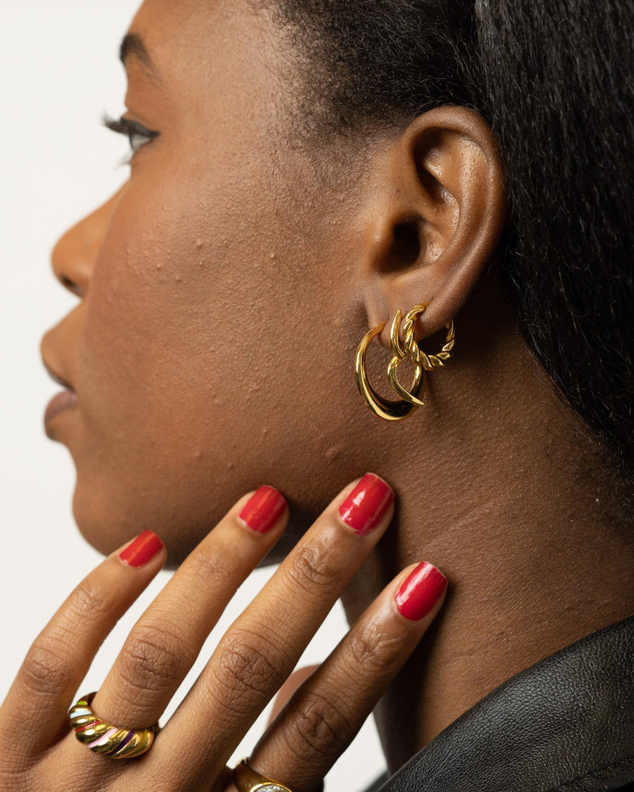 Style Image - 14K gold plated twisted hoop earrings worn on the ear with matching twisted rings visible on hand