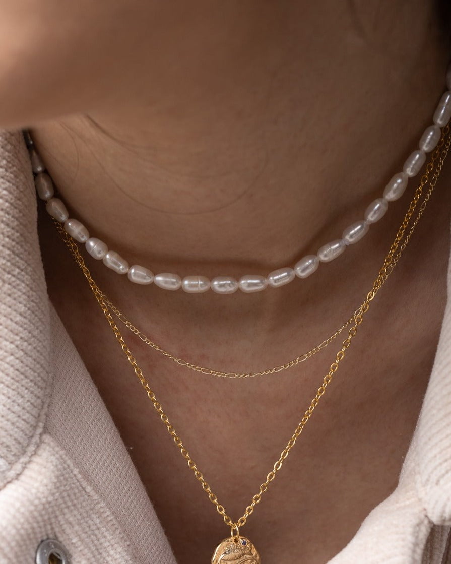 Model Image - Tiny pearl necklace layered with delicate gold chain necklaces at the neckline worn on model