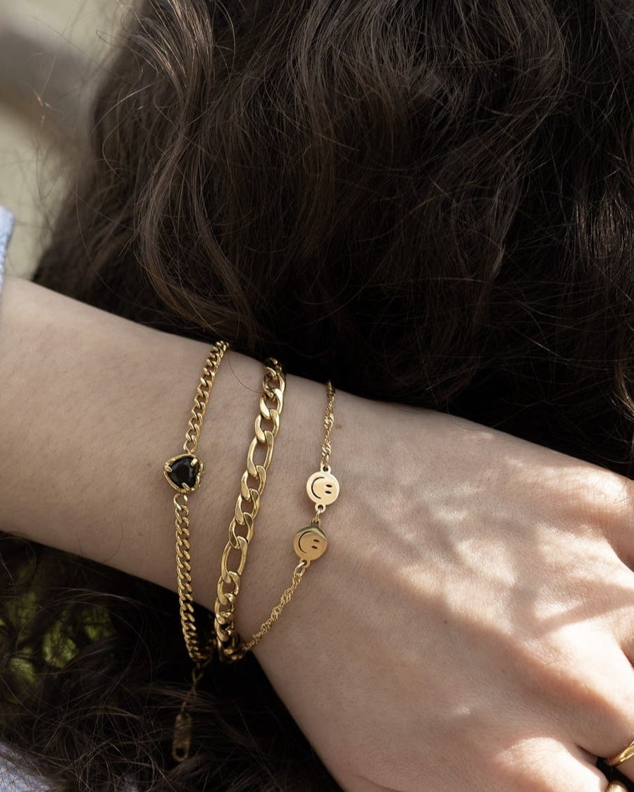 Model Image - Mini Heart Bracelet with black heart charm layered with gold-toned bracelets on the wrist worn on model