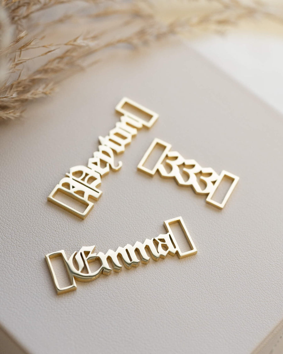 Detail Image - Customizable shoe lace name charms in 18k gold finish arranged on a neutral surface