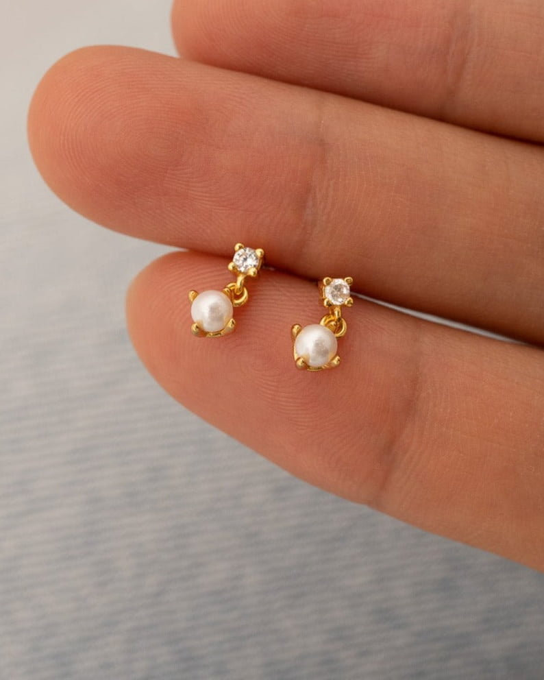 Detail Image - Diamond pearl drop stud earrings shown on fingertips for scale, with 3 x 3 mm CZ diamond and pearl accents in 14K gold plated 925 sterling silver