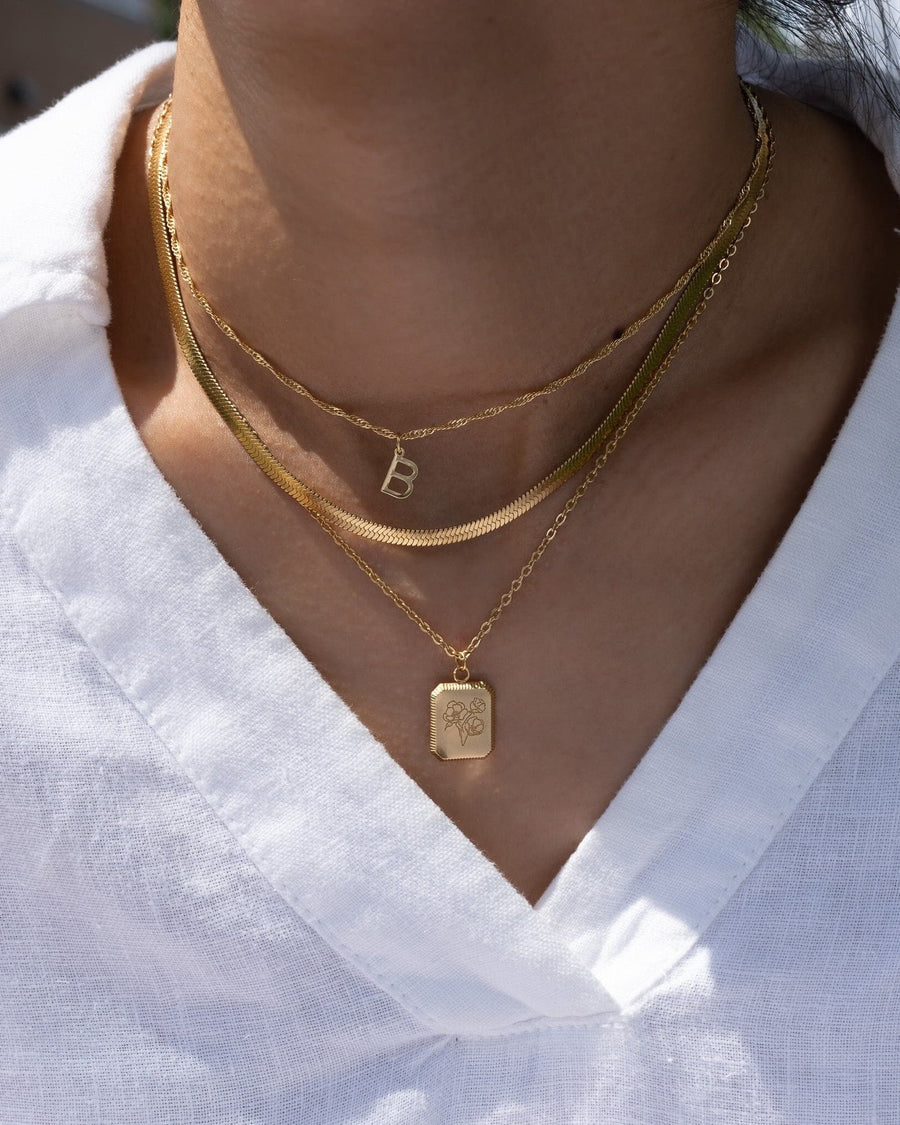 Model Image - layered initial necklace, herringbone chain, and square birth flower pendant styled together worn on model