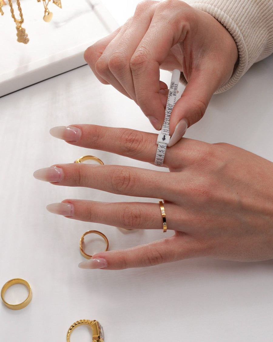 Model Image - Flexible plastic ring sizer wrapped around a finger to measure US ring size, with rings nearby, worn on model
