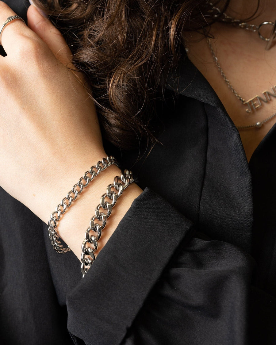 Model Image - silver Cuban chain bracelet with interlocking links styled on the wrist with layered jewelry worn on model