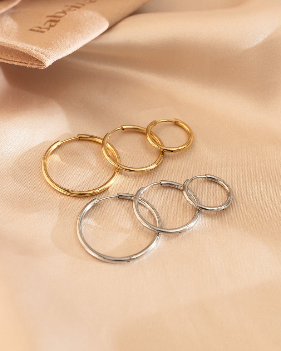 Detail Image - Hoop earrings in gold and silver tones shown in small, medium, and large sizes on soft fabric.