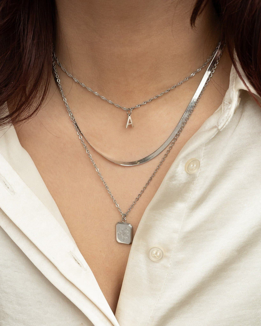 Model Image - Silver three-piece layering necklace set with initial necklace, herringbone chain, and square birth flower pendant worn on model