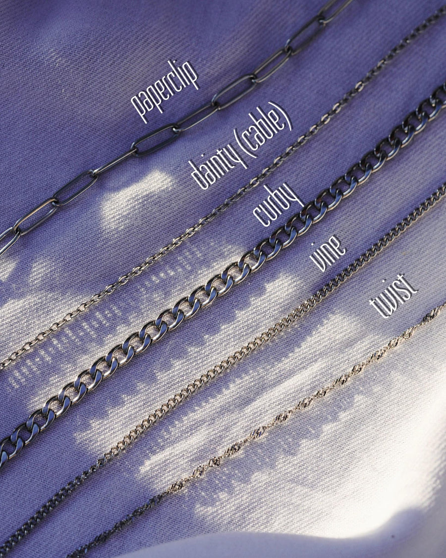 Style Image - Silver cable chain bracelet shown with other labeled chain styles on purple fabric.
