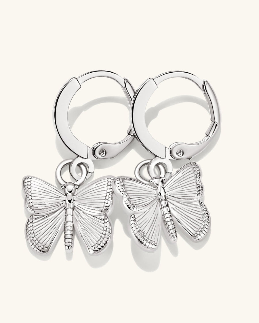 Detail Image - Dainty butterfly hoop earrings in silver finish on brass with butterfly charms on a light background