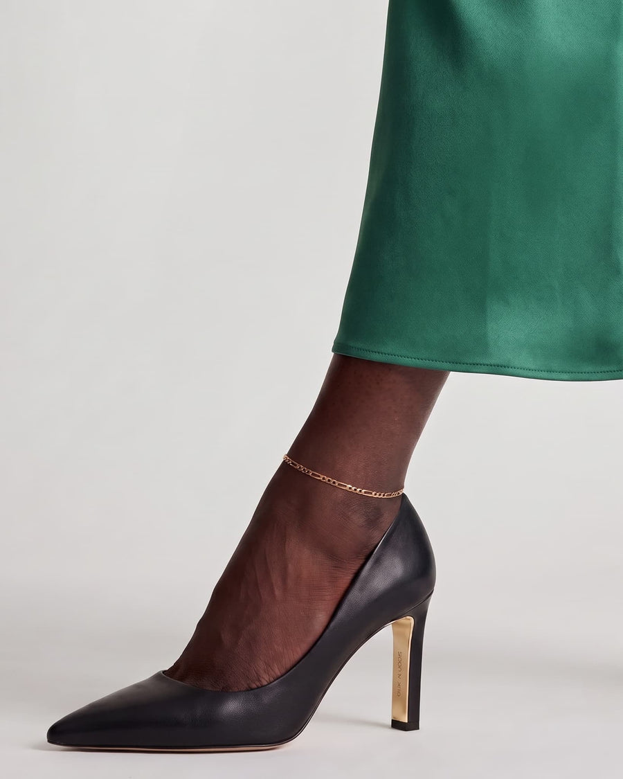Model Image - 14K gold Figaro anklet with 3 mm links styled at the ankle above a black heel and green hem worn on model