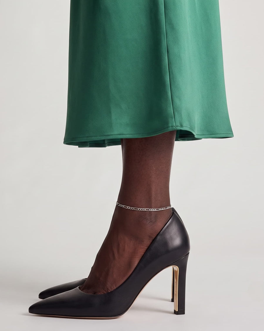 Model Image - Rhodium Figaro anklet styled around the ankle with a green dress and black heel worn on model