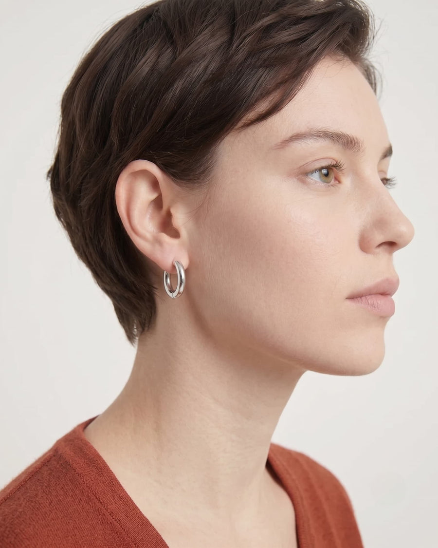 Model Image - Silver-toned simple 12mm hoop huggie earring shown on the ear in a side profile worn on model