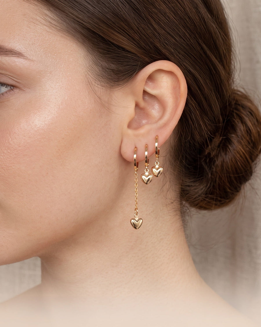 Style Image - 14K Gold puffy heart hoop earrings worn in an ear stack with dangling heart charms and chain detail