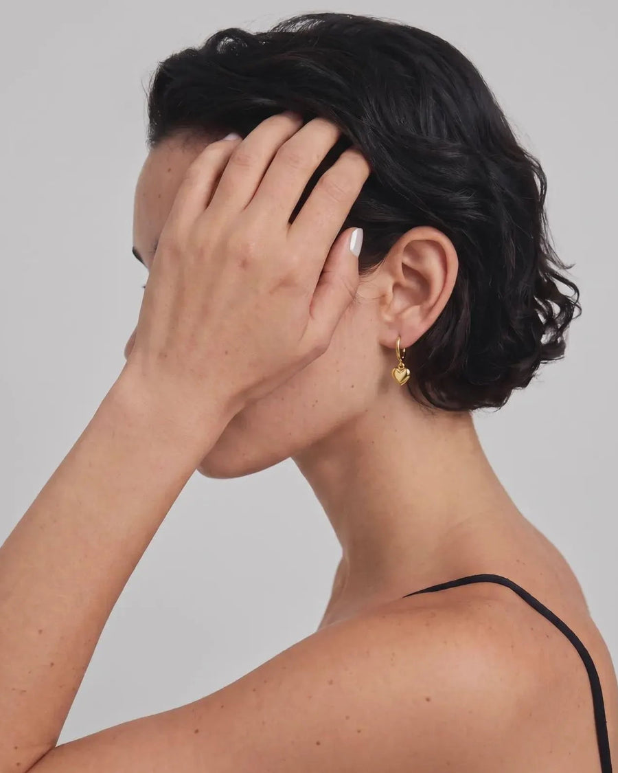 Model Image - 14K gold hoop earring with dangling puffy heart charm worn on model