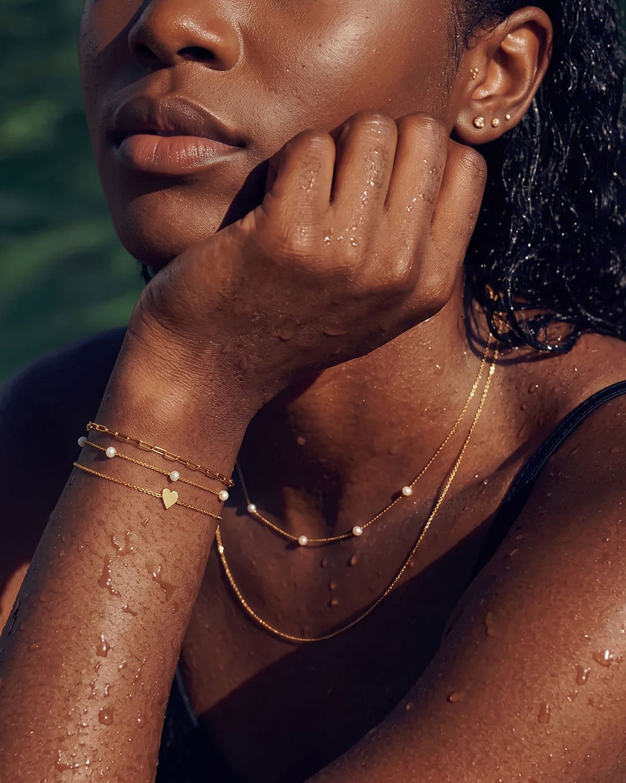 Model Image - 14k solid gold engravable heart bracelet with delicate chain and heart-shaped pendant layered on the wrist worn on model