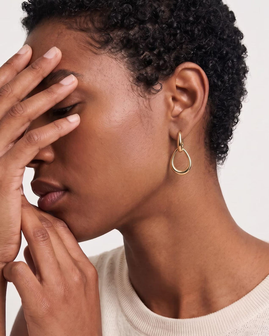 Model Image - 14K gold teardrop hoop earring with an open silhouette shown on the ear worn on model