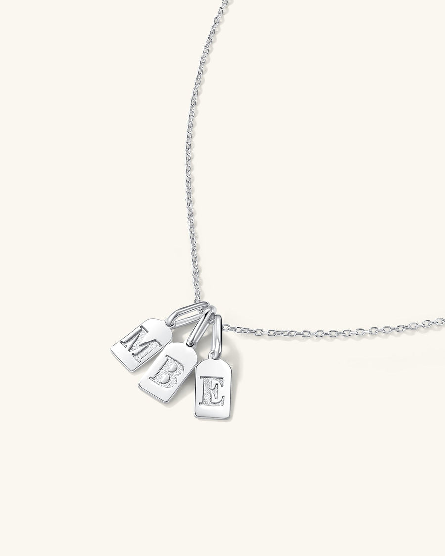  Dainty initial tag charms with engraved letters layered on a delicate necklace worn on model