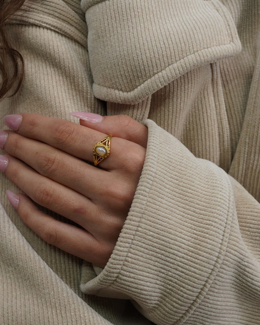 Model Image- A close-up of a person's hand wearing a gold ring with a white oval stone, resting on a beige ribbed cardigan.