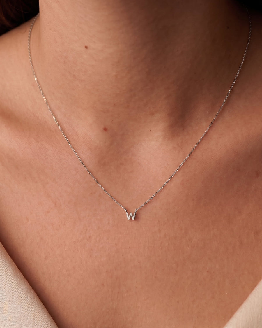 Model Image - A delicate silver chain necklace with a small initial 'W' pendant, worn on the neck of a model.