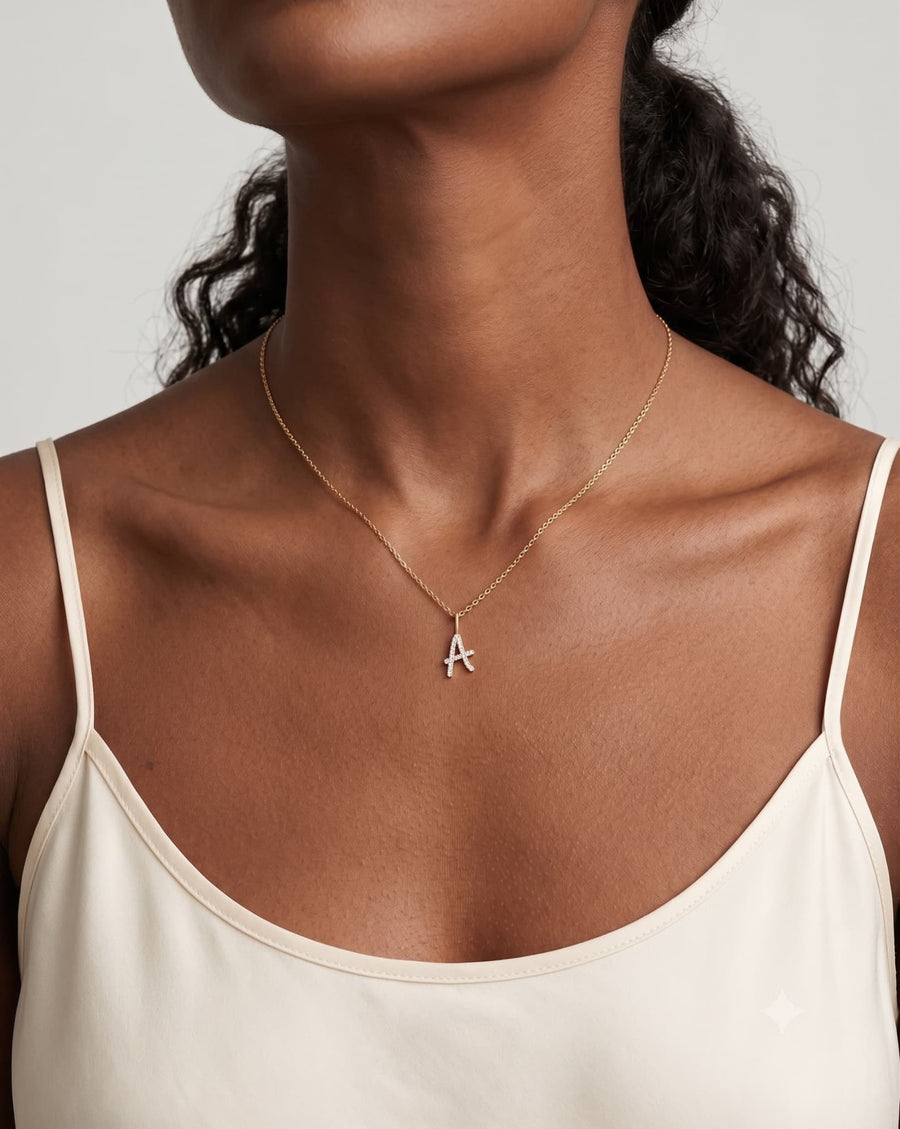 Model image - A close-up of a model wearing a delicate gold chain necklace with a small silver initial 'A' pendant, styled with a cream camisole top against a light gray background.