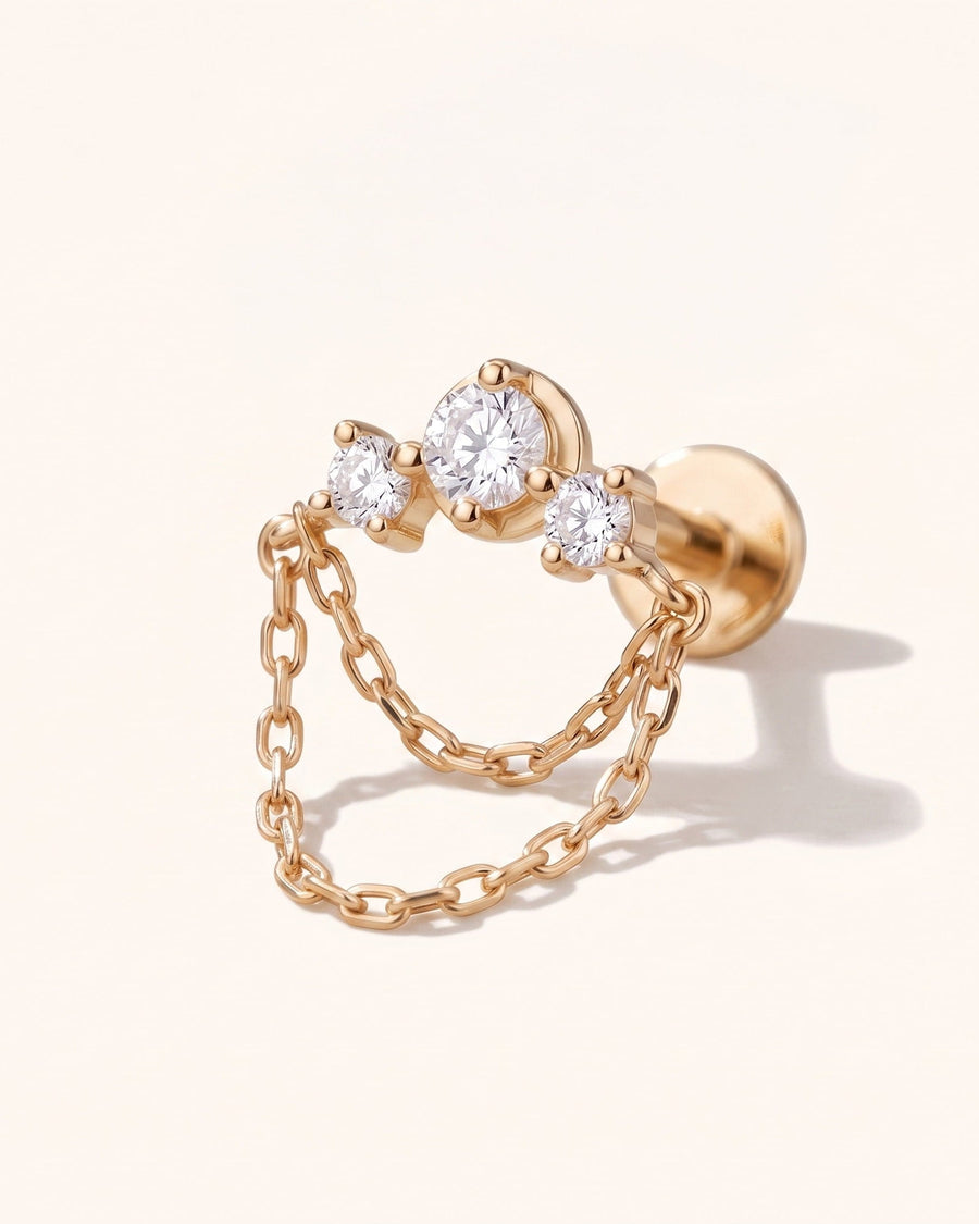 A rose gold double-hoop earring with three clear round-cut gemstones on the front and a delicate chain draped between the hoops, shown on a light cream background.
