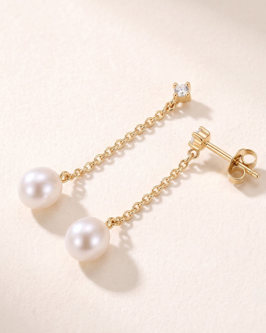 Detail Image - 14k solid gold pearl drop earrings with round natural white sapphires and fine diamond-cut chain on a warm neutral background.