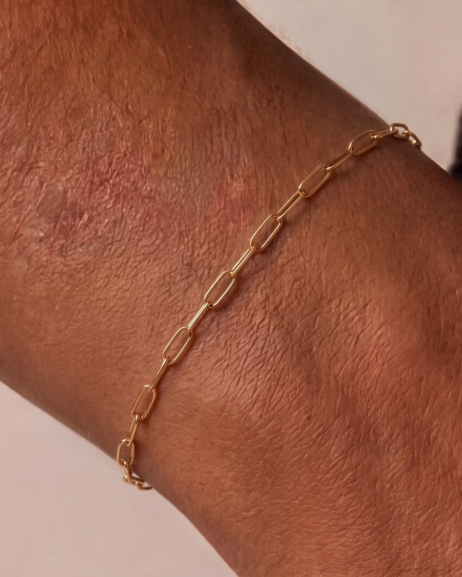model image - A delicate gold paperclip chain bracelet worn on a person's wrist, shown in a close-up shot against a neutral light background.